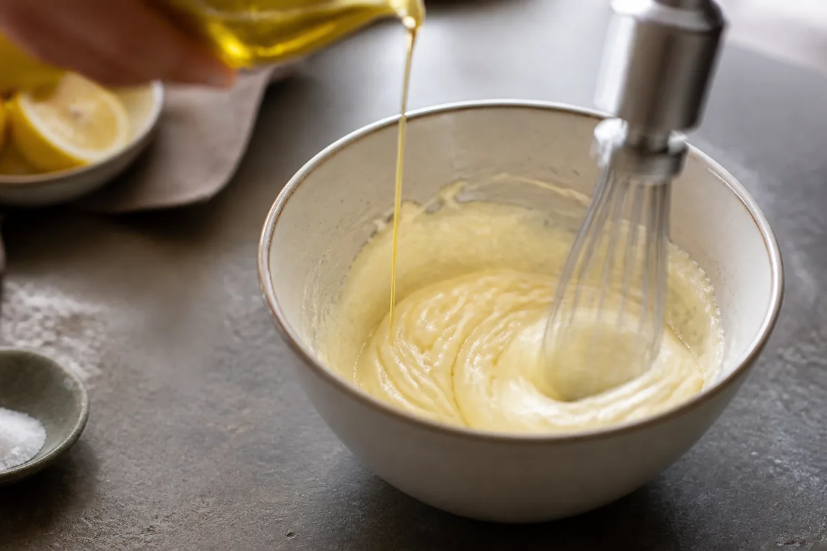 Bol étroit avec une mayonnaise en cours de montage et un filet d&rsquo;huile versé lentement